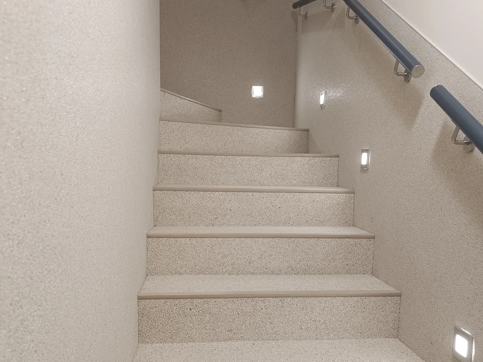 Escalier intérieur recouvert de pierre claire, marches, contremarches et murs, main courante et lumières encastrées