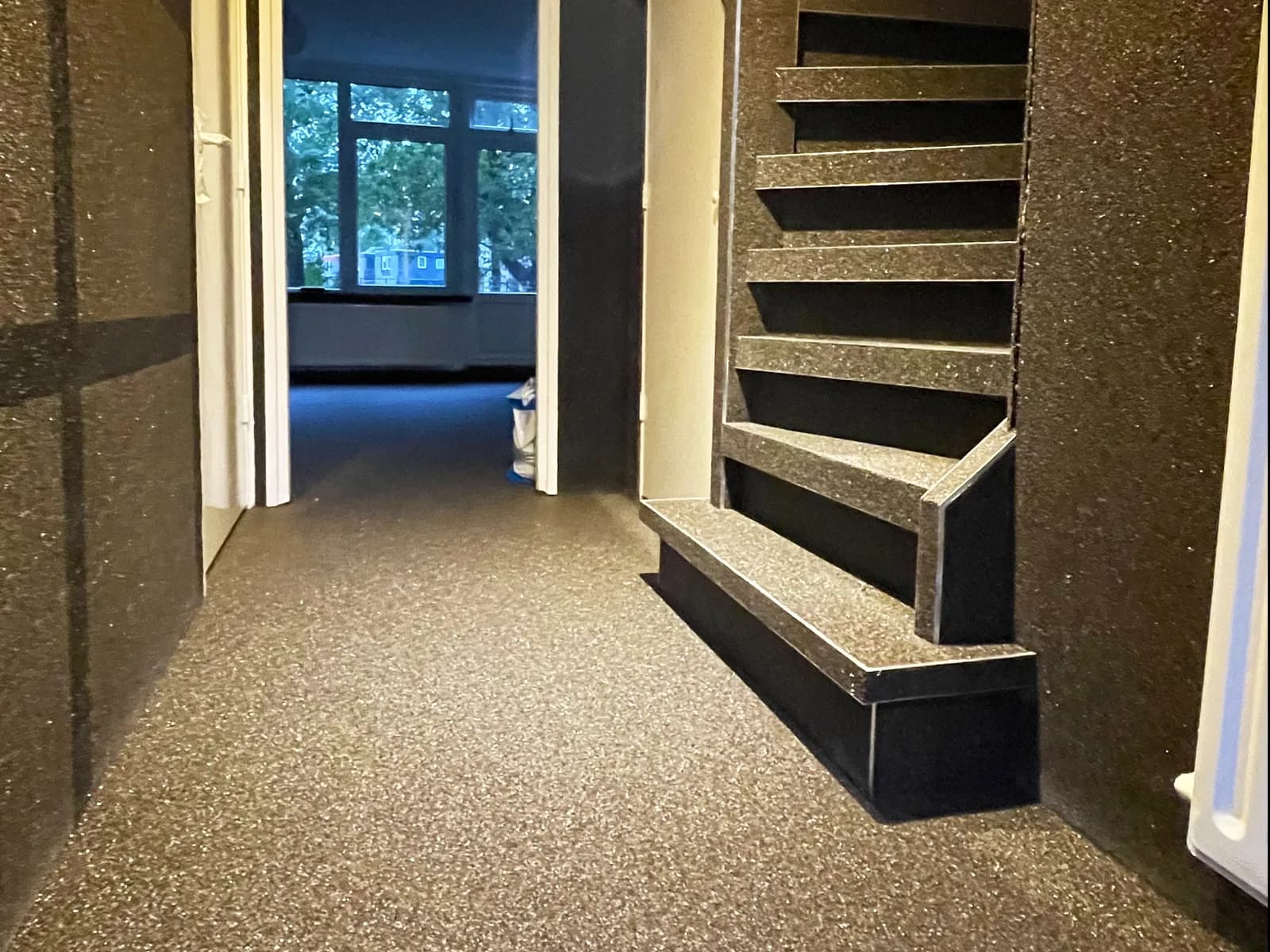 Couloir au plancher de pierre foncée continu, qui se prolonge sur les marches d’un escalier tournant