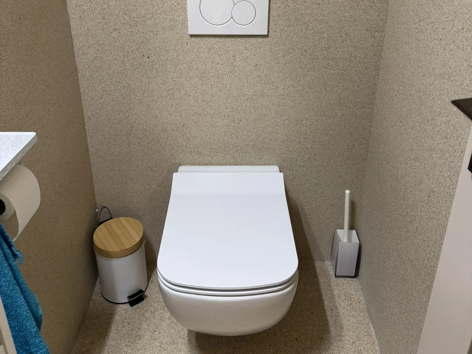 Toilette suspendue dans une petite salle d’eau dont le sol et les murs sont recouverts de pierre beige continue