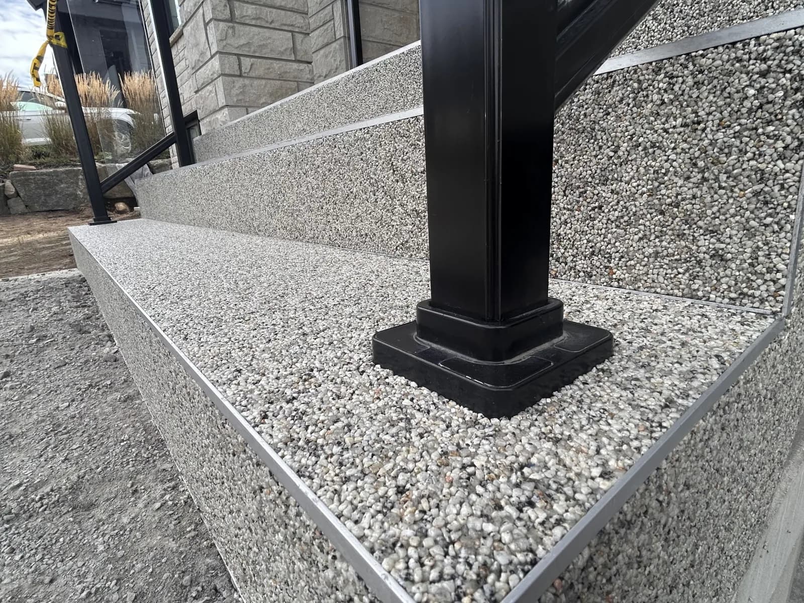 Le coin d’une marche : la tranche recouverte comme le dessus, bordée d’un profilé d’aluminium, au pied d’un poteau de garde-corps