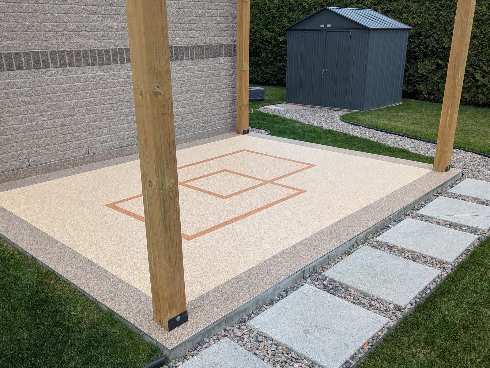 Terrasse sous pergola recouverte de granulux clair, deux carrés entrecroisés en terre cuite, bordure sur le pourtour
